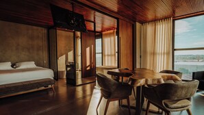 Habitación de hotel moderna con una cama grande, una mesa de comedor con sillas y vistas a la ciudad.