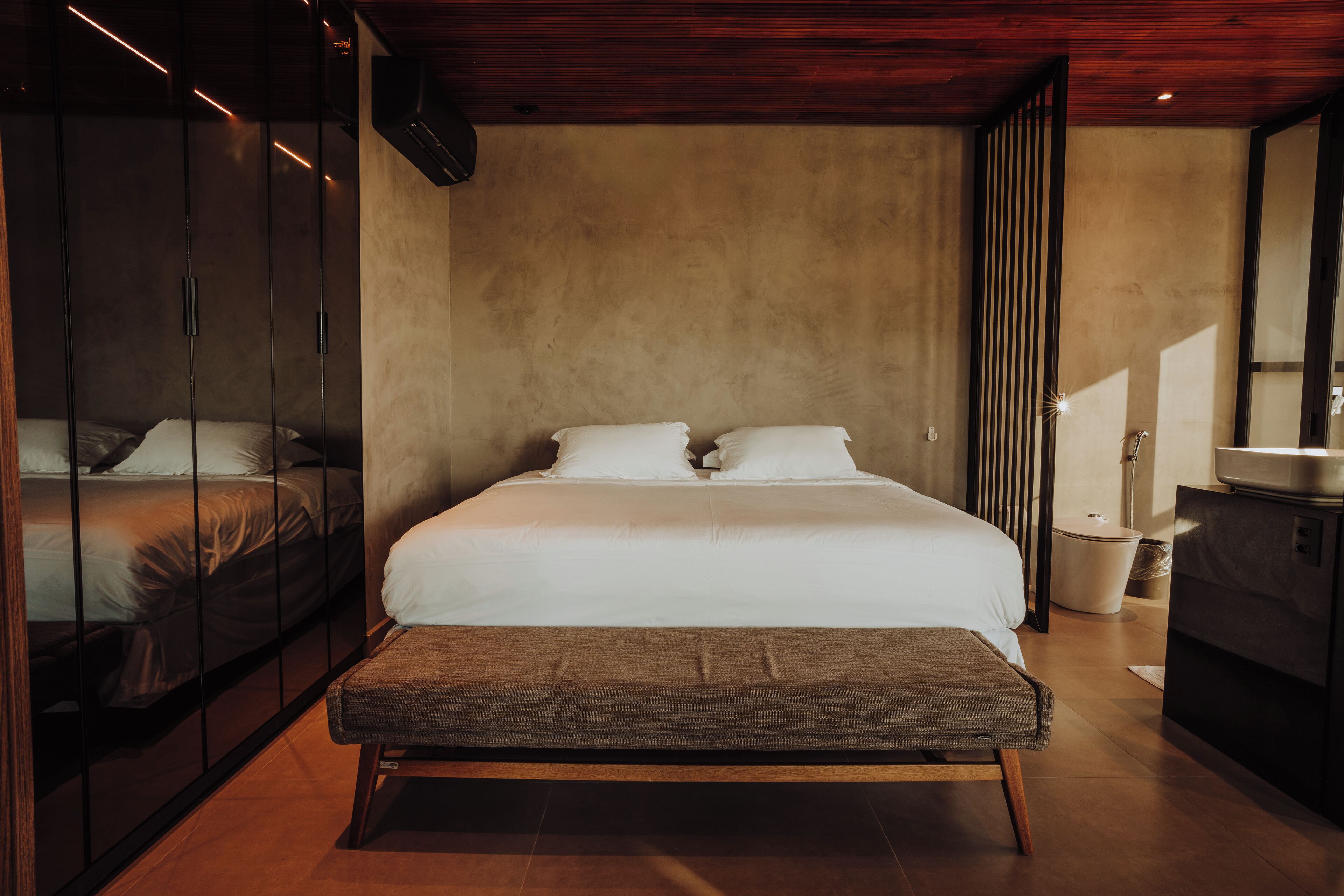 A modern bedroom with a large bed, a bench, and a wardrobe.