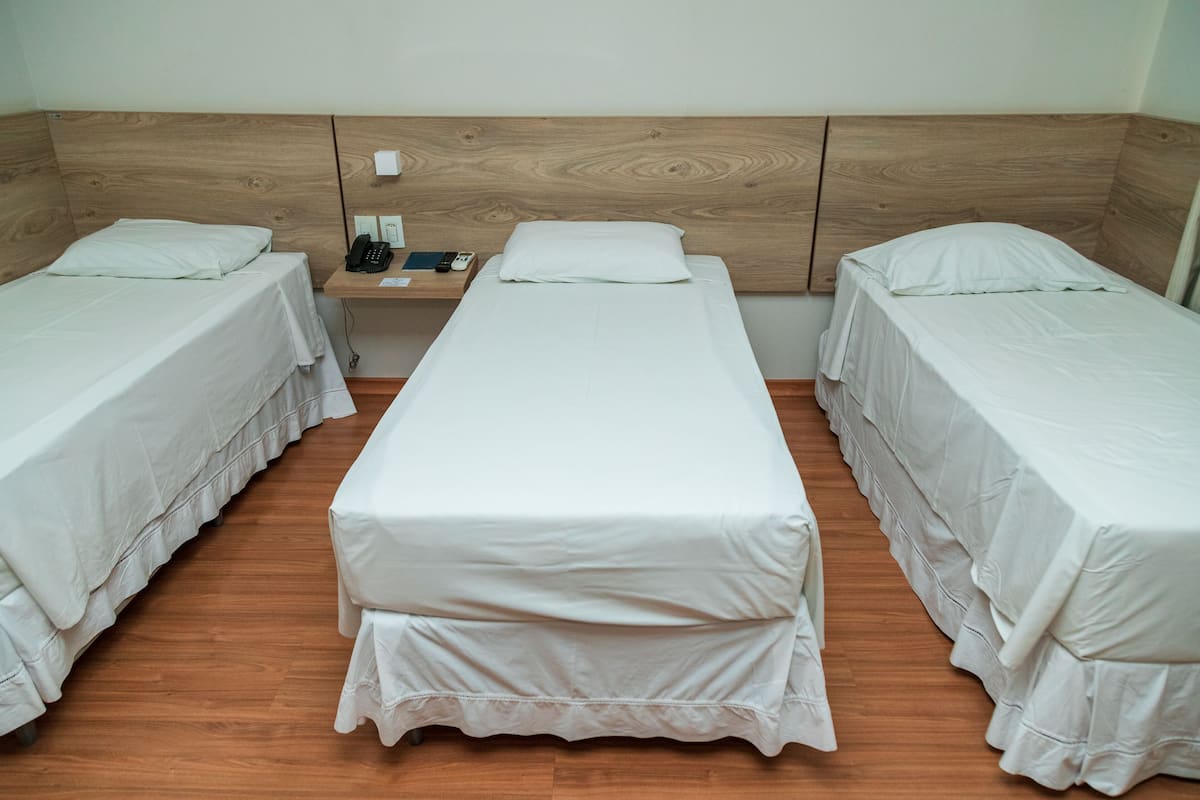 A room with three single beds aligned in a row, each with a wooden headboard and white bedding.