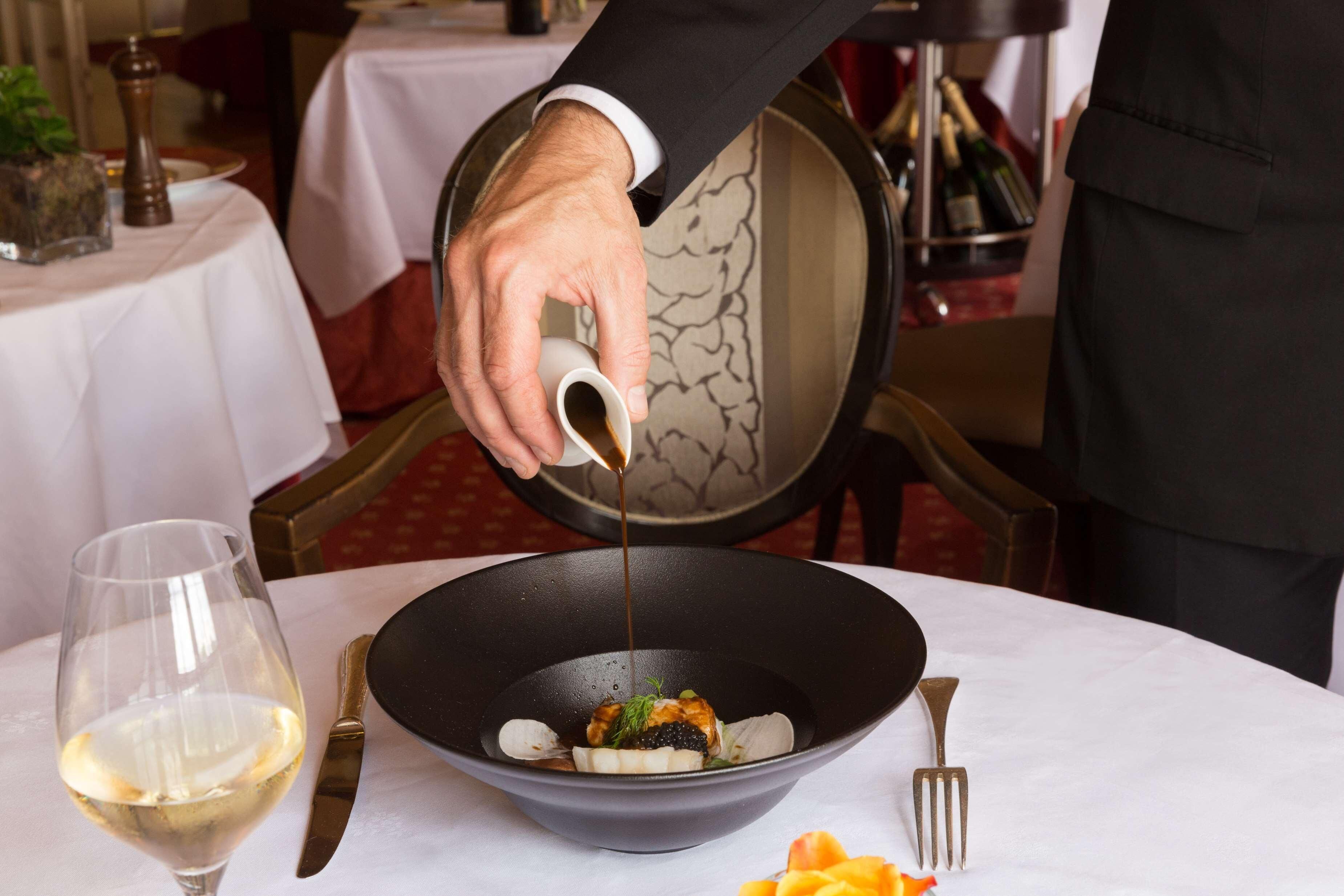 A person pouring a sauce into a bowl on a table.