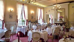 Un comedor con mesas redondas, sillas, candelabros y cortinas.