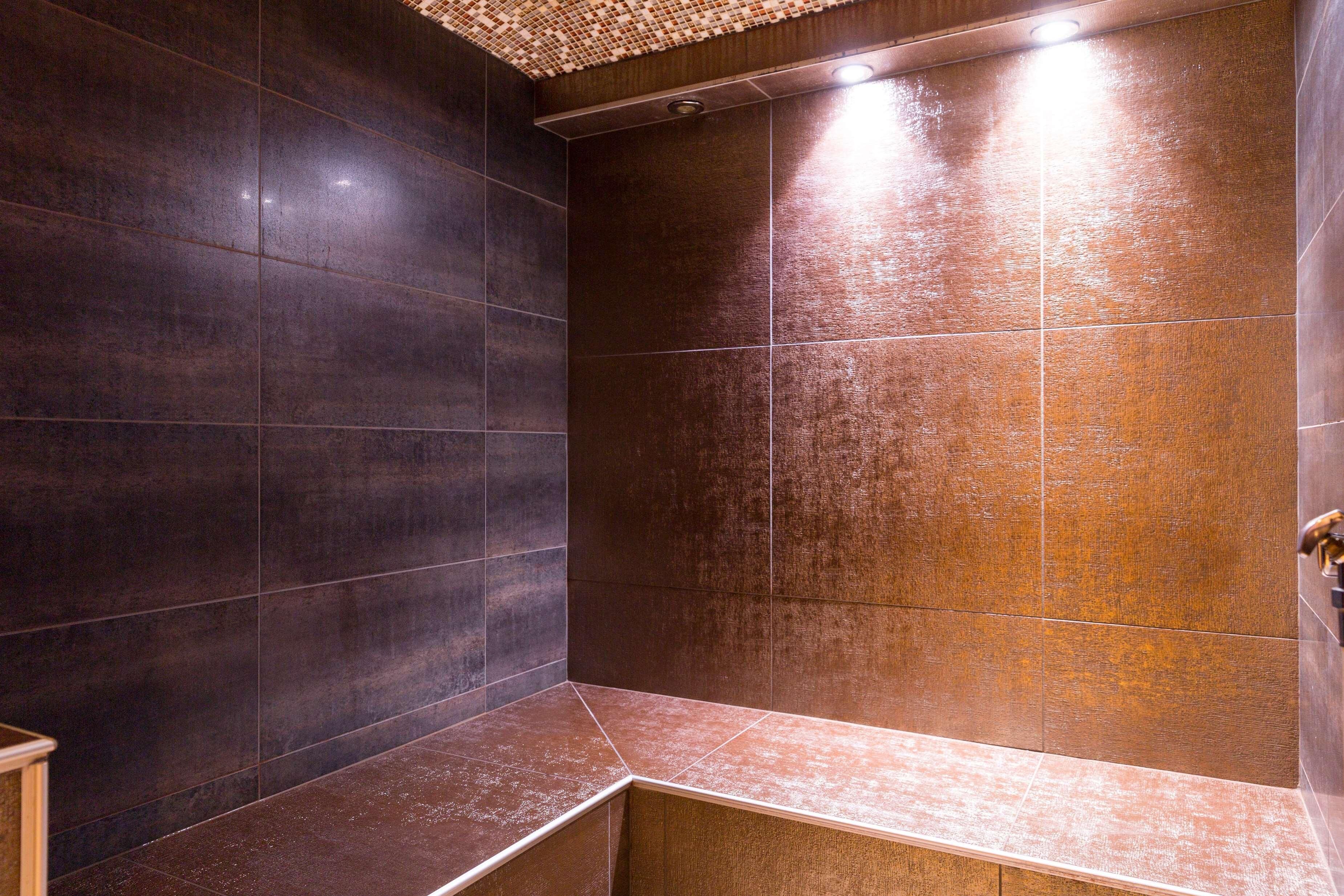 A modern bathroom with dark tiles and a wooden bench.