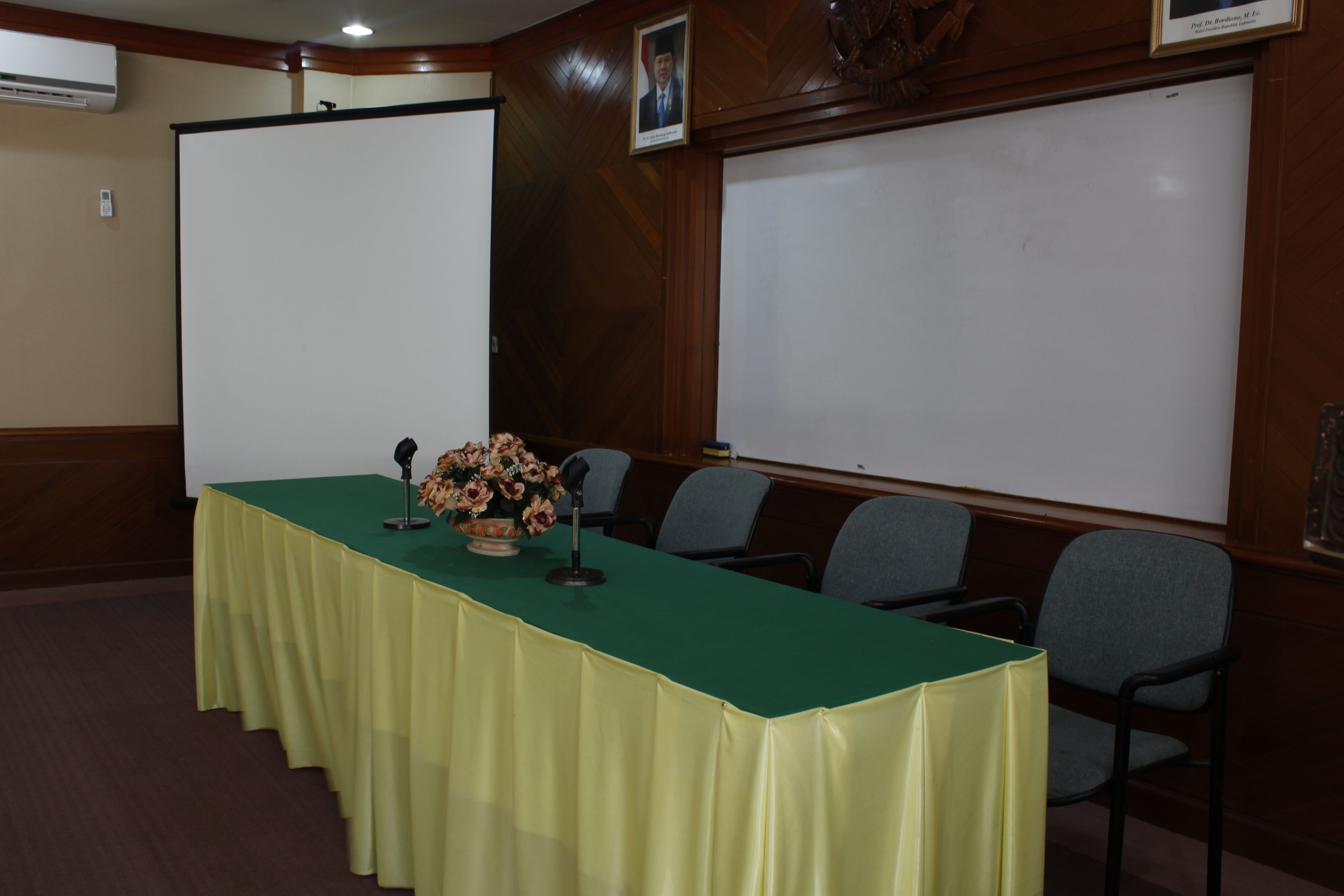 Un salón de conferencias con una larga mesa, sillas, una pantalla de proyector y una pizarra.