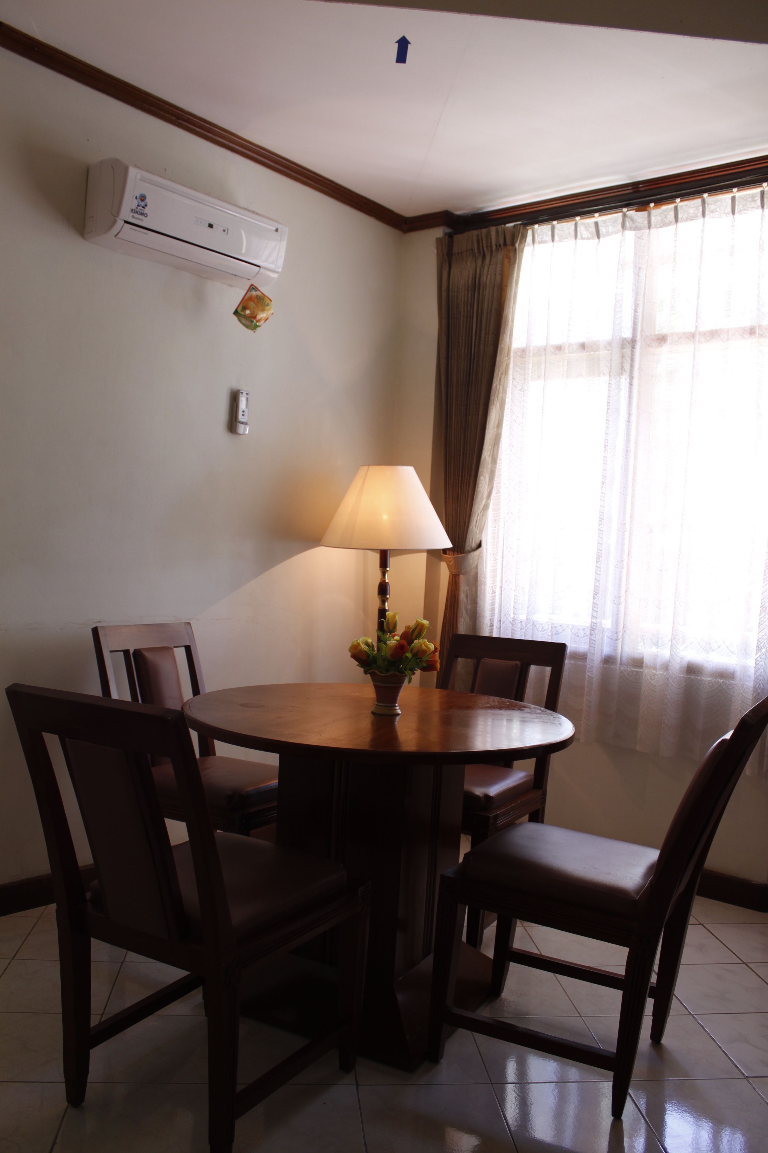 A dining area with a round table, four chairs, a lamp, and an air conditioning unit on the wall.