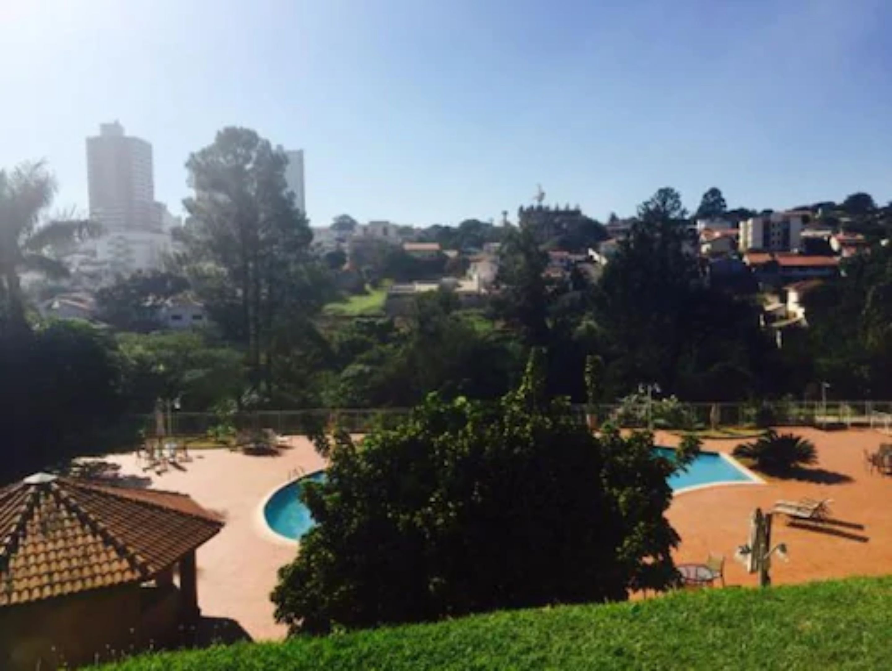 A view of a residential area with a swimming pool, a small building with a tiled roof, and a tall building in the background.