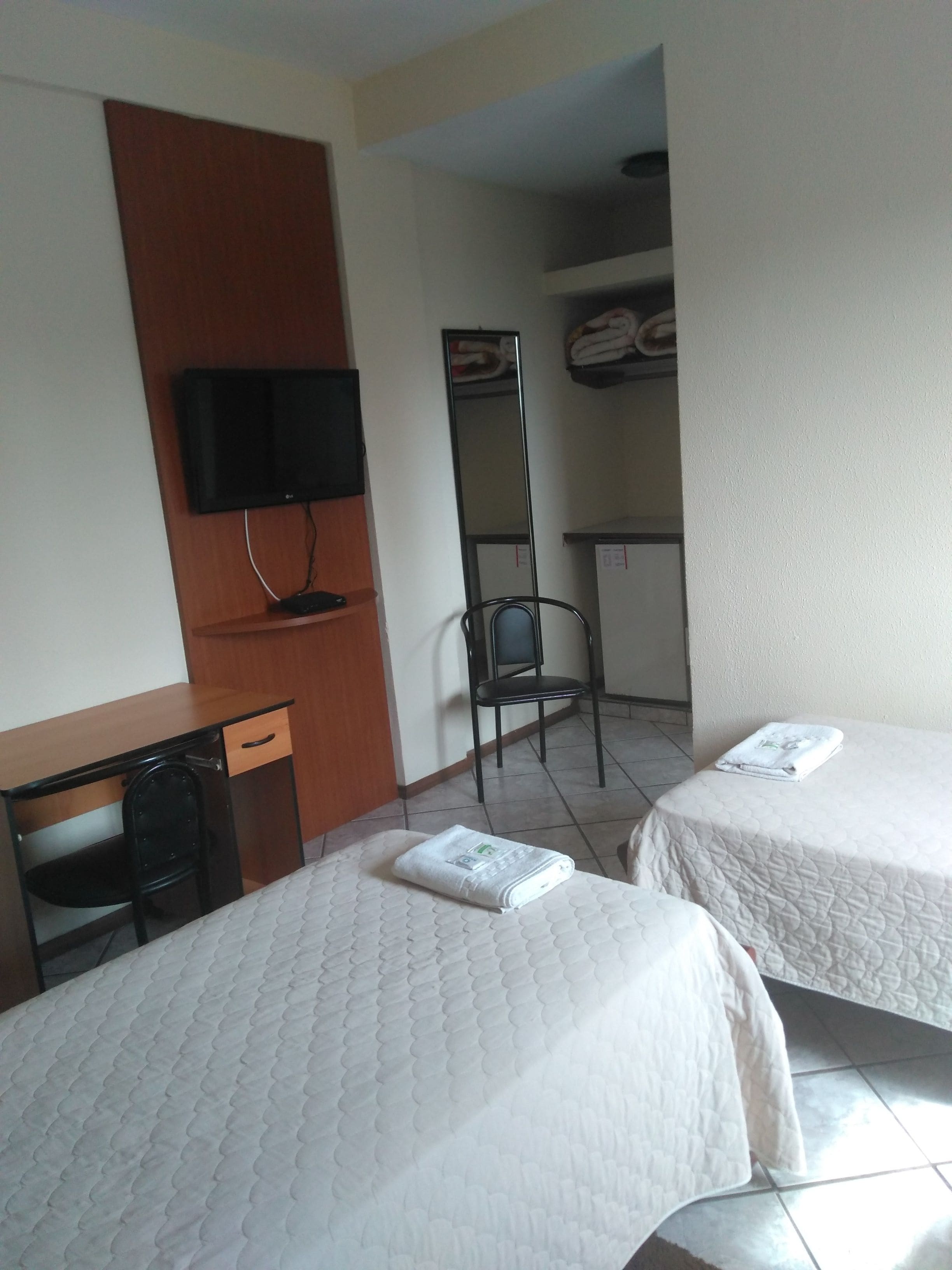 Ett hotellrum med två sängar, ett skrivbord, en stol, en TV och en spegel.