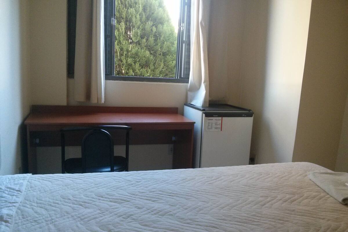 Una habitación con una cama, un escritorio, una silla y un refrigerador pequeño.