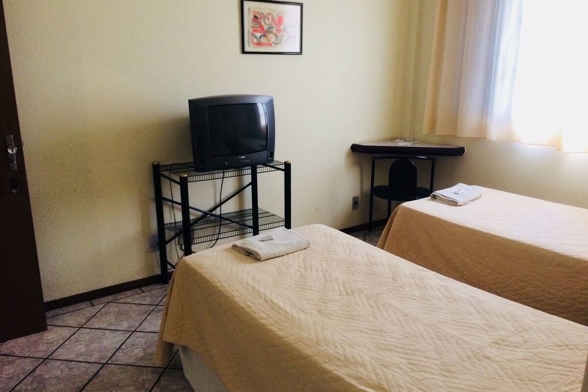 Habitación de hotel con dos camas, un televisor en un mueble bajo, una mesita y un cuadro en la pared.