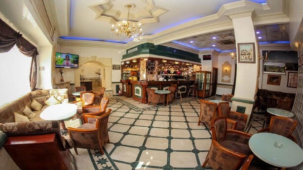 Vestíbulo de hotel con zona de bar, arreglos de asientos y una araña.