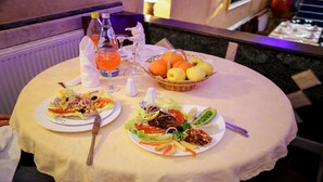 Una mesa servida con dos platos de comida, una botella de jugo de naranja y una cesta de frutas.