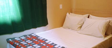 Una cama con una colcha a cuadros, una cortina verde y una pared blanca.