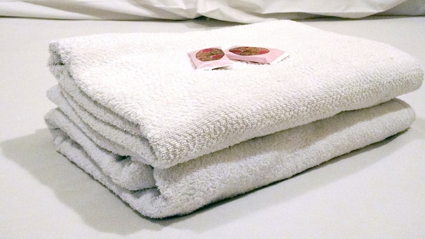 Een keurig opgevouwen witte handdoek op een bed, met twee kussens op de achtergrond.