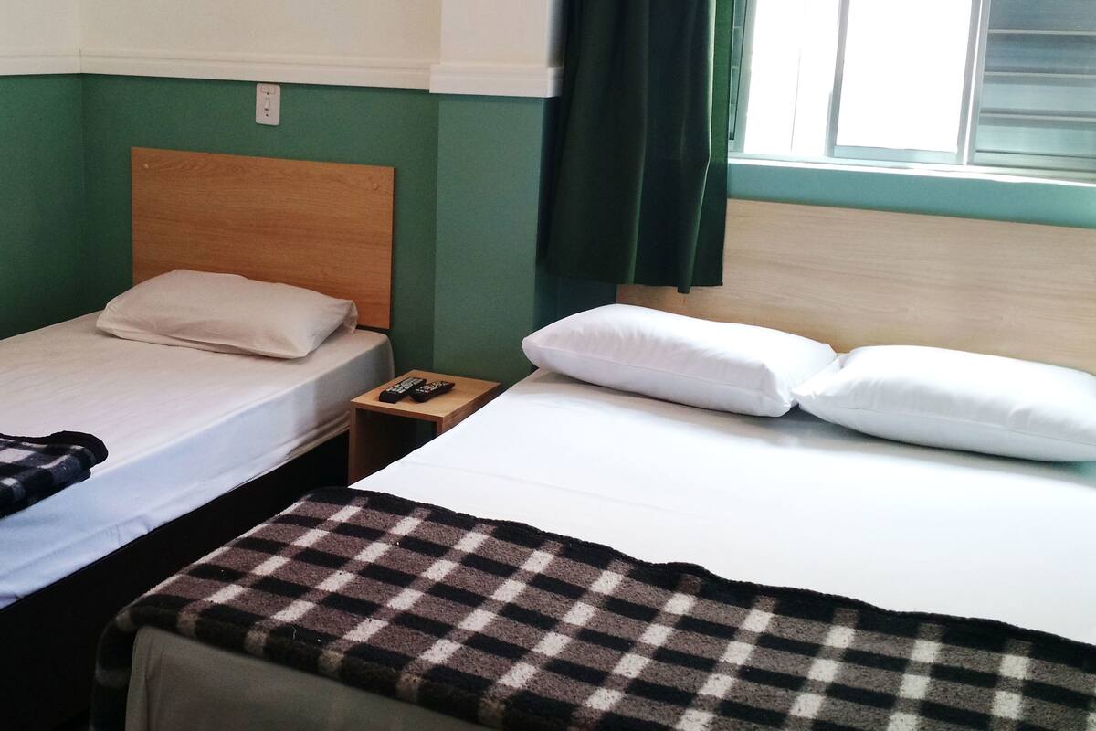 Een kamer met twee bedden, een nachtkastje, een geruit dekbed en een raam met gordijnen.