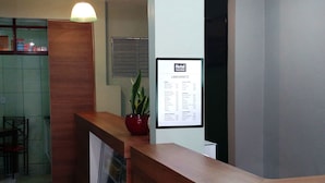 Een hotel receptie met een houten balie, een kamerplant en een menubord.