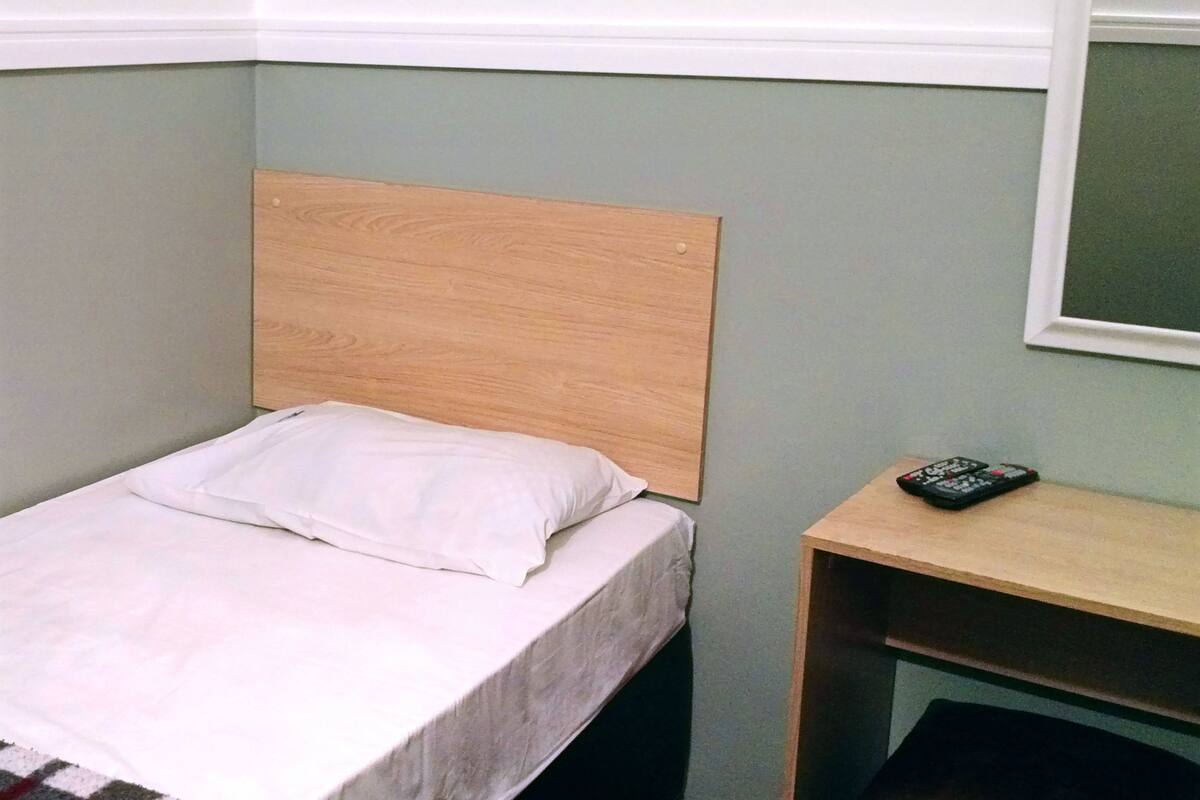 Een enkel bed met een houten hoofdbord in een kamer met lichtgroene muren.