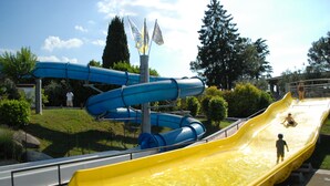 Parque acuático con múltiples toboganes, incluyendo un tobogán amarillo destacado y toboganes azules, rodeado de follaje y árboles.