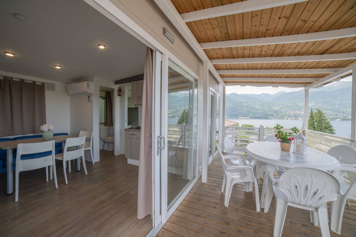 Ein geräumiger Balkon mit Holzboden, weißen Möbeln und Blick auf Berge und einen See.