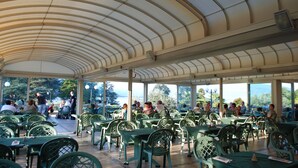 Un patio techado al aire libre con sillas y mesas verdes, ofreciendo vistas del paisaje circundante.