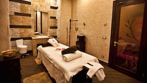 Une salle de spa équipée d’une table de massage, d’un lavabo, d’un miroir, d’un porte-serviettes et d’une fresque décorative représentant un arbre sur la porte.