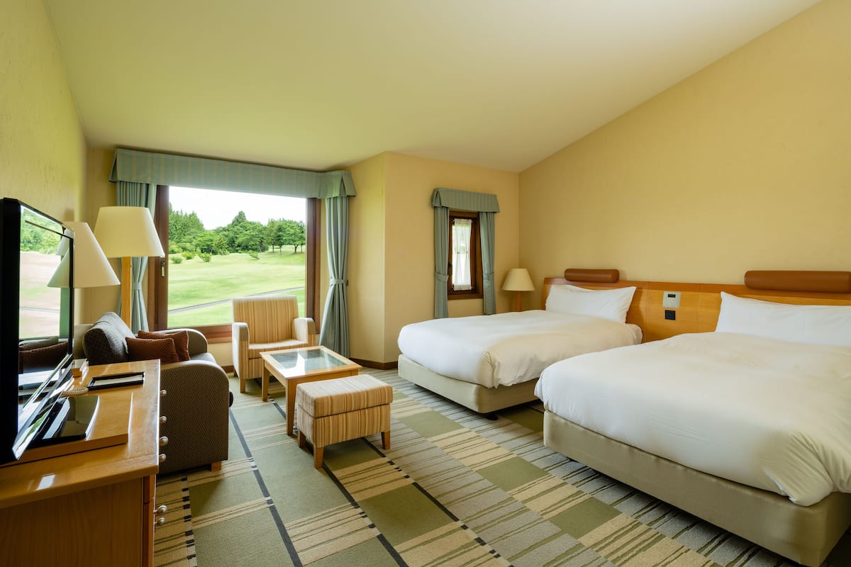 A hotel room with two beds, a TV, a desk, and a view of the outdoors.
