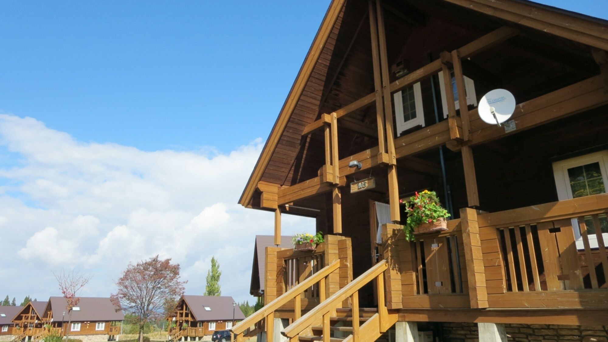 A wooden cabin with a balcony, a satellite dish, and a stone foundation.