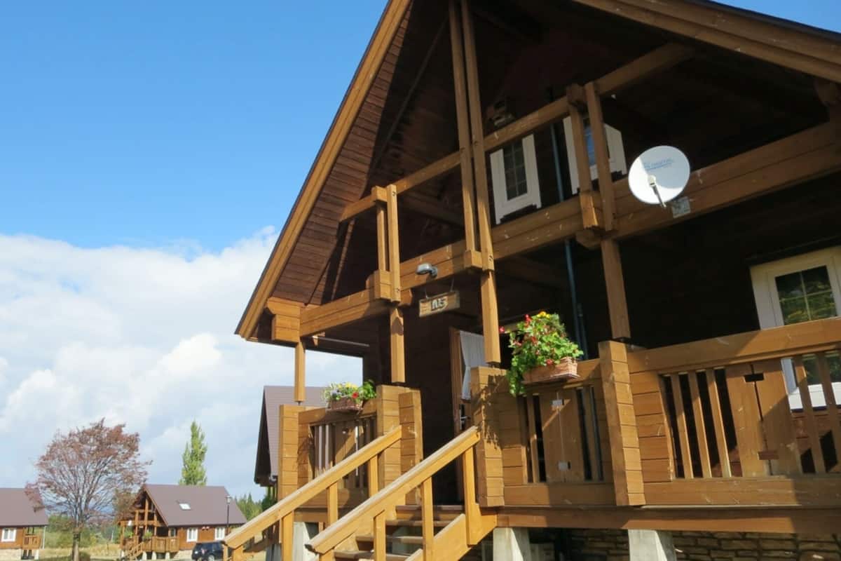 A wooden cabin with a balcony, a satellite dish, and a stone foundation.