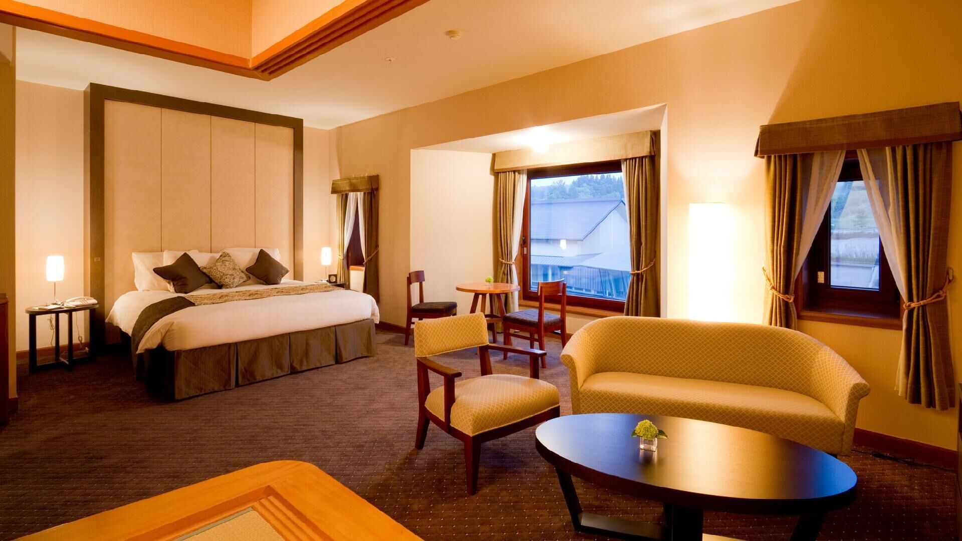 A hotel room with a bed, two chairs, a sofa, a small table, and a window with curtains.