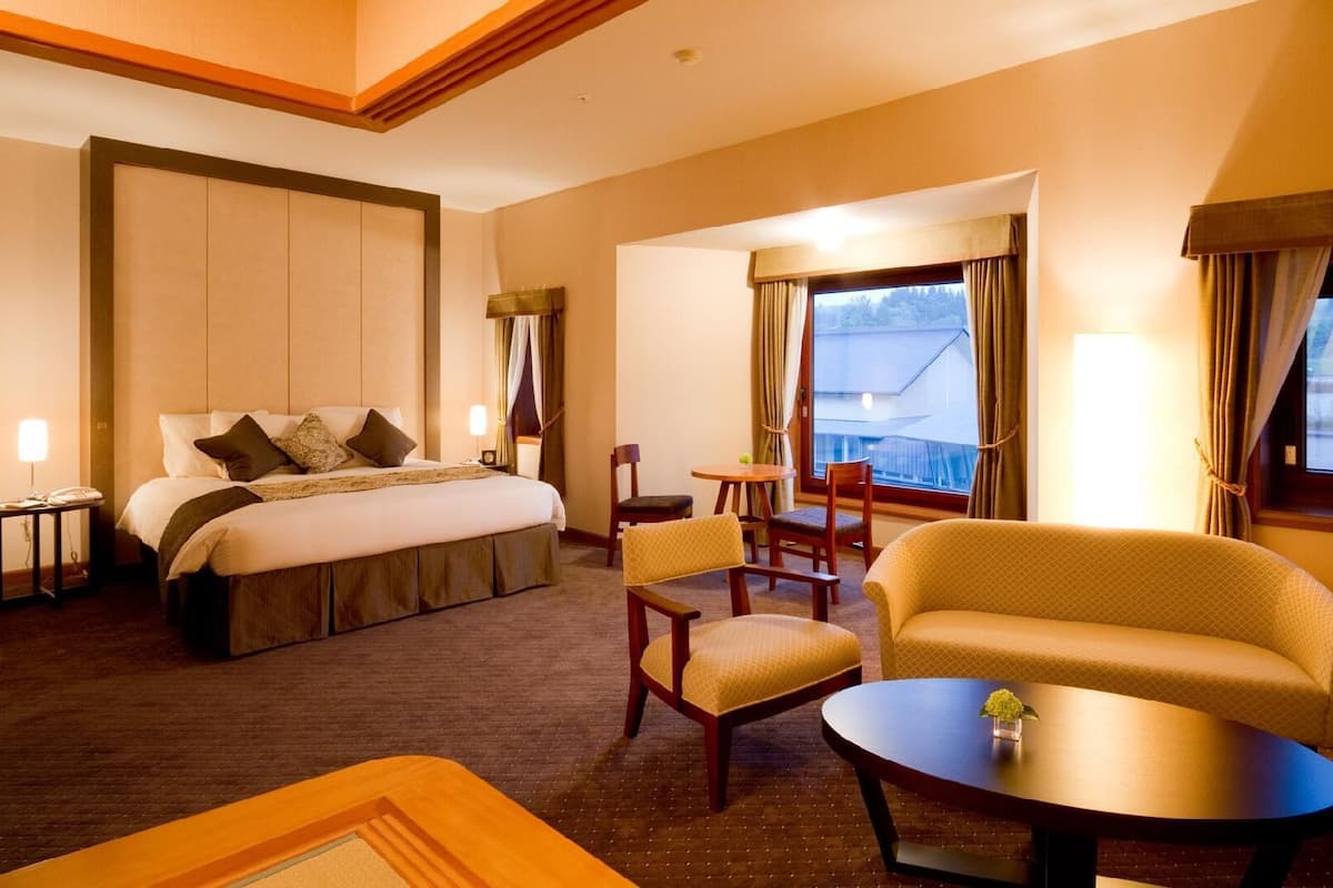 A hotel room with a bed, two chairs, a sofa, a small table, and a window with curtains.