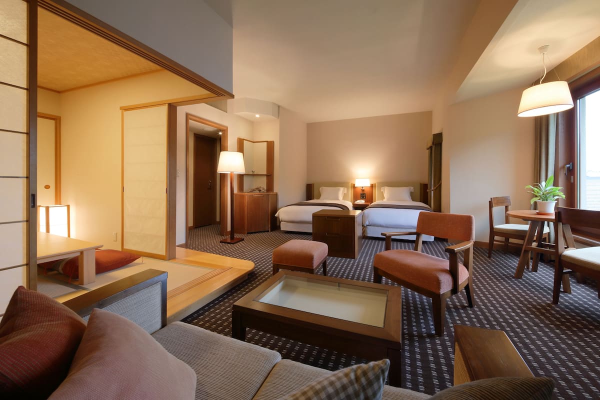 A hotel room with a bed, two bedside tables, a sofa, a coffee table, and a small dining area with chairs and a table.