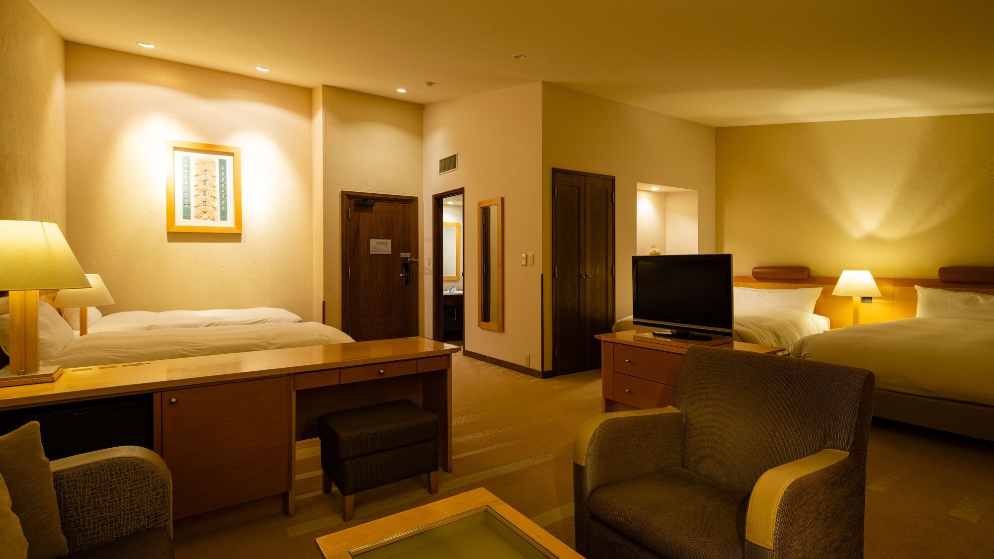 A hotel room with a bed, desk, chair, television, and a bathroom visible through an open door.