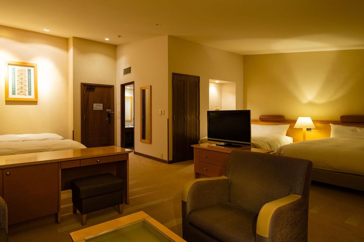 A hotel room with a bed, desk, chair, television, and a bathroom visible through an open door.