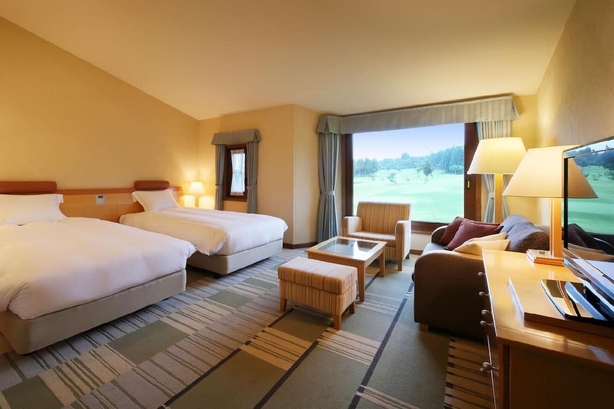 A hotel room with two beds, a sofa, a TV, and a view of a golf course.