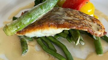 A plate with a piece of fish, green beans, and a slice of tomato.