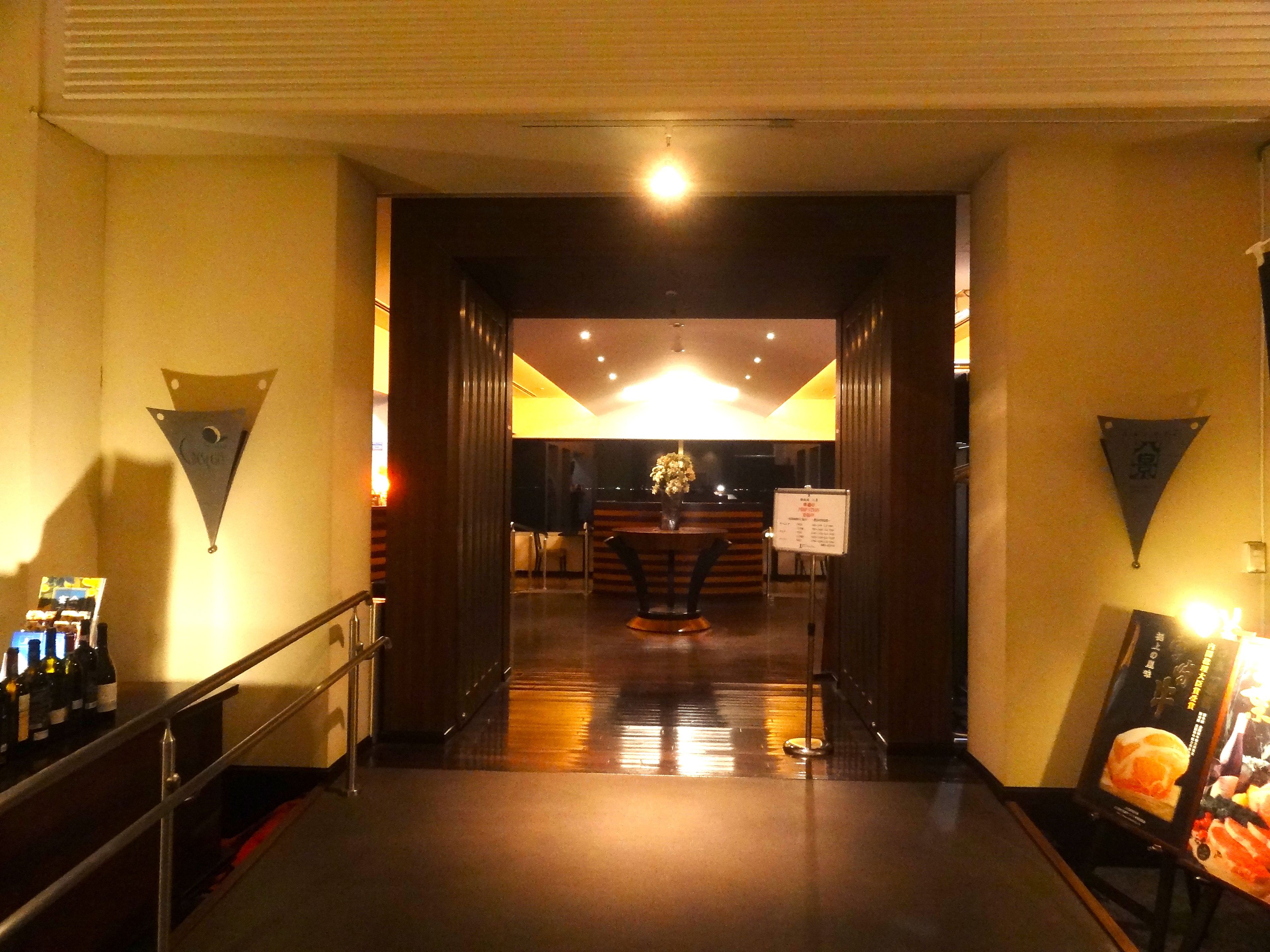 Um saguão de hotel com uma mesa de recepção, uma escadaria e um quadro de menu fixado na parede.