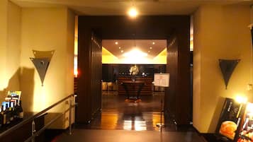 Um saguão de hotel com uma mesa de recepção, uma escadaria e um quadro de menu fixado na parede.