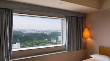 Een hotelkamer met een groot raam met uitzicht op de stad, een bedlampje en een net opgemaakt bed.