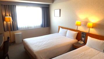 Een hotelkamer met twee bedden, een bureau, een stoel, een lamp en een raam met gordijnen.