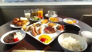 Una mesa de desayuno con diversos platos, como croissants, arroz y fruta, ubicada en un balcón con vista a la ciudad.