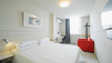 A hotel room with a large bed, a desk, a chair, and a red armchair.