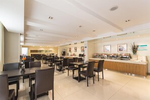 Un comedor de hotel moderno con múltiples mesas y sillas, una barra central con dispensadores de comida y un interior limpio y bien iluminado.