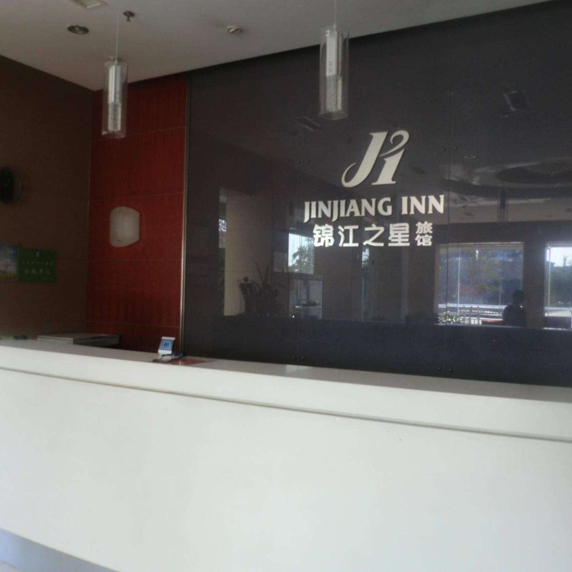 A reception desk with a sign for JINJIANG INN and a reflection of a person in the window.
