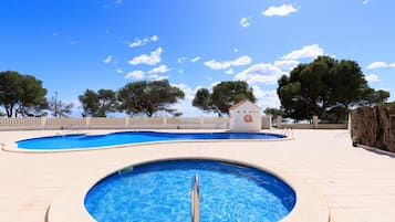 Zona de piscina con un pequeño edificio y árboles al fondo.