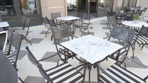 Uma área externa com mesas e cadeiras, dispostas em um padrão com cadeiras alternadas em preto e branco.