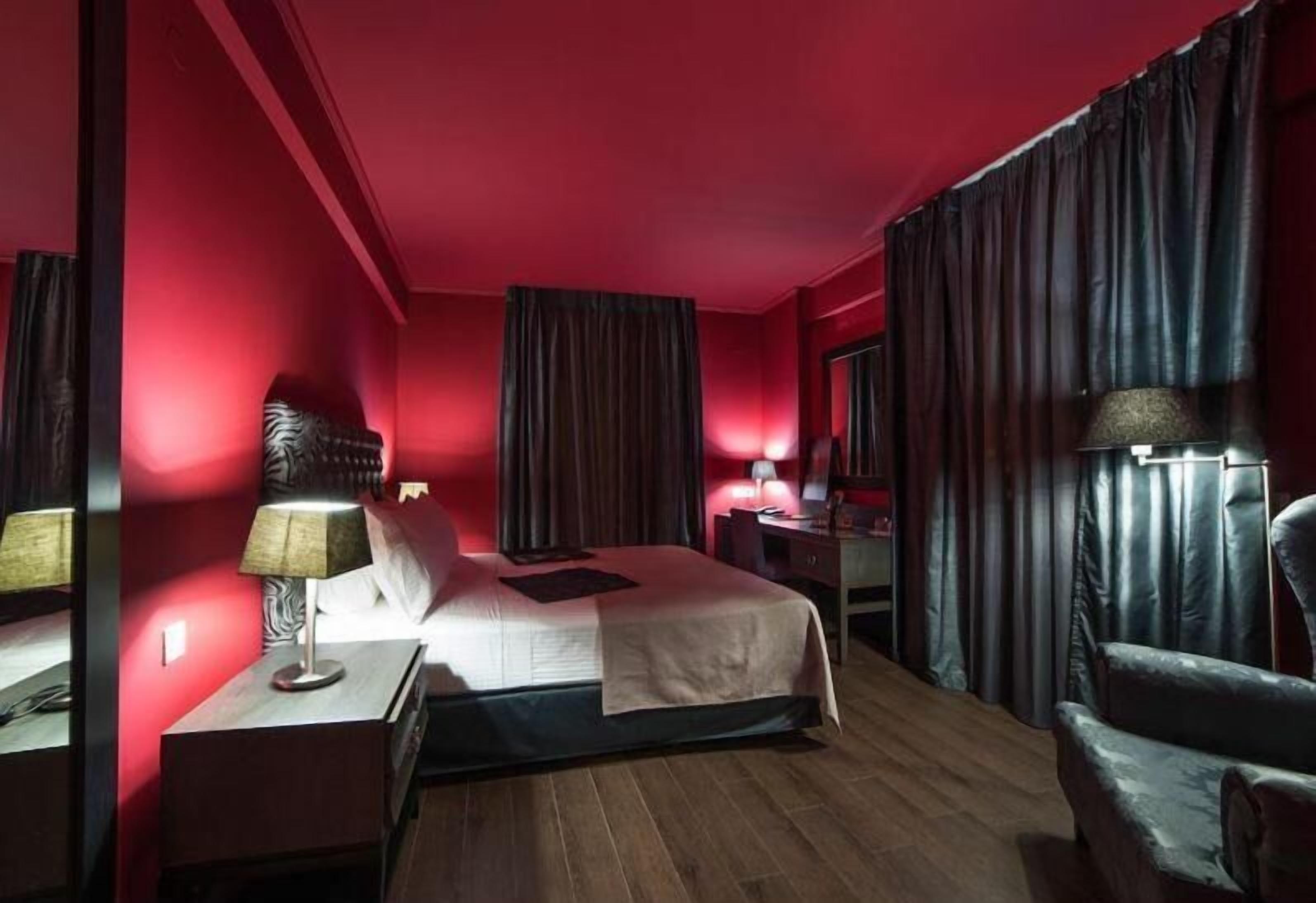 A hotel room with a large bed, a desk, a chair, and a nightstand with lamps.