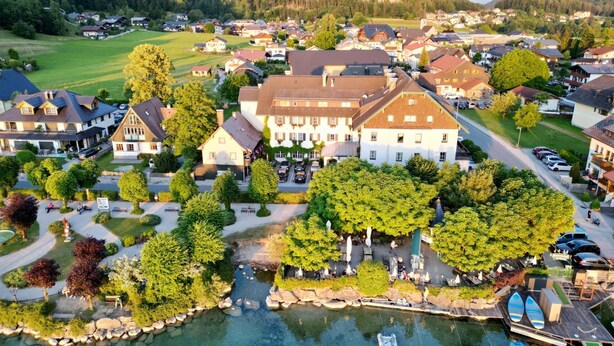 A riverside town with a prominent white building, a small dock with boats, and a lush green landscape. - Seehotel Schlick (Fuschl am See)