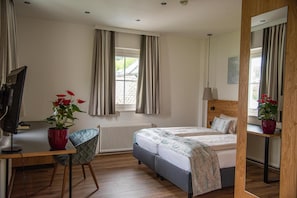 A bedroom with a bed, a desk, a chair, a radiator, and a window with curtains. - Seehotel Schlick (Fuschl am See)