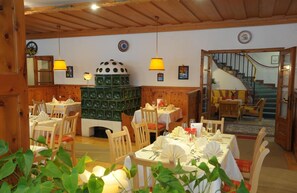 A cozy restaurant with wooden interiors, a central green stove, and a staircase leading to an upper level. - Seehotel Schlick (Fuschl am See)