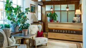 A reception area with a wooden desk, a reception sign, and potted plants. - Seehotel Schlick (Fuschl am See)