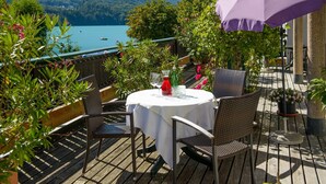A round table with a white tablecloth, surrounded by wicker chairs, set on a wooden deck with a view of a lake and mountains. - Seehotel Schlick (Fuschl am See)