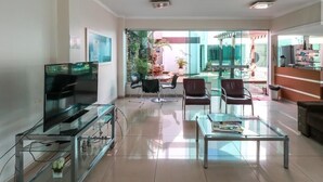 Un salon moderne avec un téléviseur à écran plat posé sur un meuble en verre, une table basse en verre et deux fauteuils en cuir.